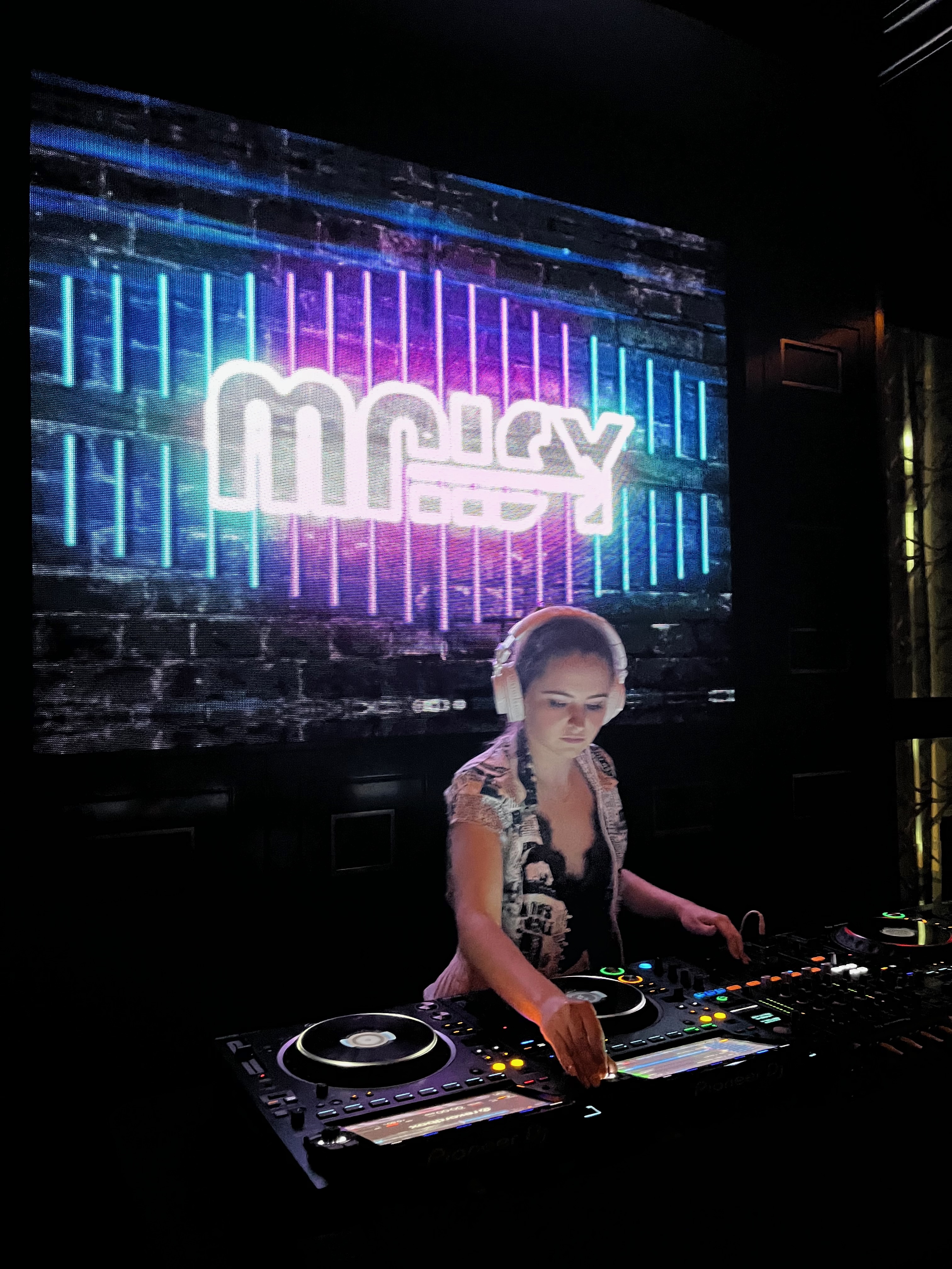 Maisy DJing under club lighting with her name on the screen